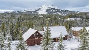 Une cabane dont le toit est recouvert de neige, entourée d’une forêt et avec une montagne en arrière-plan.
