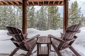 A wooden gazebo with two Adirondack chairs and a table, surrounded by snow-covered trees. - Elk Creek | Ski-In/Out + Peloton! (Big Sky)