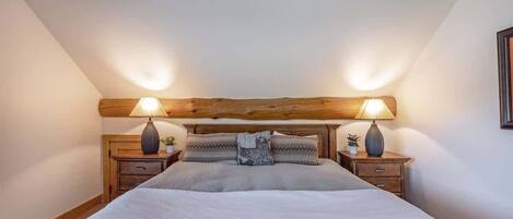 Een slaapkamer met een houten hoofdbord, twee nachtkastjes met lampen, een bed met een grijze deken en twee kussens.
