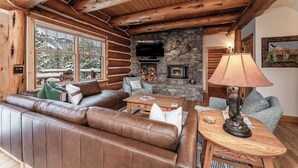 L’intérieur d’une cabane en rondins, avec un canapé en cuir, une cheminée, un téléviseur et une lampe.