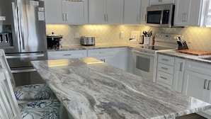 A modern kitchen with white cabinetry, a marble island, and pendant lighting.