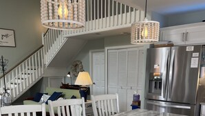 A kitchen with a marble countertop, white cabinetry, a stainless steel refrigerator, and a staircase with white railings.