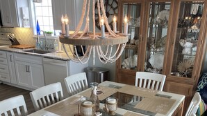 A dining area with a long table, white chairs, and a chandelier.