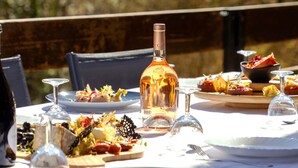 Une table à manger installée à l’extérieur, avec une bouteille de spiritueux, des assiettes remplies de nourriture et des verres à vin.