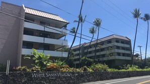 A multi-story building with a stone wall in front labeled "WHITE SANDS VILLAGE." - Stunning ✨ Comfortable and Well Decorated Property 🌺 Incredible Views! 🏖 White Sands 318 (Kailua Kona)