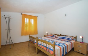 Quarto com cama de madeira, mesa de cabeceira, luminária, janela com cortinas e um cabideiro.