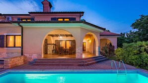 Une maison à deux étages avec une piscine, comprenant un espace repas extérieur et une cheminée en pierre.