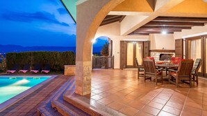 Un espace aménagé au bord de la piscine, avec un coin repas, des piliers en pierre et une vue sur les montagnes.