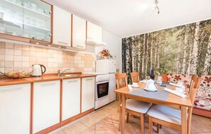 A compact kitchen with white cabinets, a built-in oven, and a dining area with a wooden table and chairs.