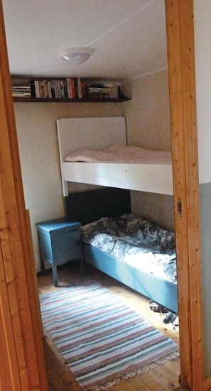 A narrow room with a bunk bed, a small bedside table, and a striped rug on the floor.