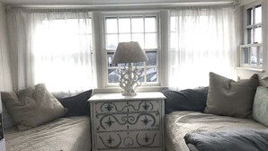 Una camera accogliente con un letto, un comodino bianco con una lampada e una finestra con tende trasparenti.
