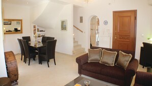Ein Wohnzimmer mit einem braunen Sofa, einem Esstisch mit Stühlen, einer Treppe und einer Holztür.