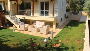 Ein zweistöckiges Haus mit überdachter Terrasse, Gartenmöbeln und einer Treppe, die zum oberen Stock führt.