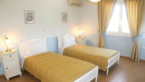 Ein Zimmer mit zwei Betten, einem Nachttisch mit Lampe, einer Klimaanlage und einem Fenster mit Vorhängen.
