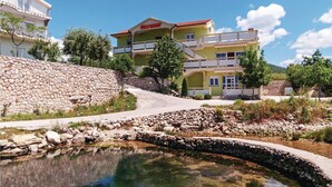 A multi-story building with balconies, a stone wall, and a clear water feature in front. - Nice Home in Ribnica-krusevo With Wifi and 1 Bedrooms (Obrovac)
