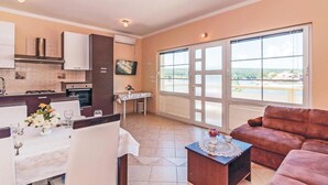 A modern living room with a sofa, a dining area with a table set for two, and a kitchen with a stove and cabinets. - Nice Home in Ribnica-krusevo With Wifi and 1 Bedrooms (Obrovac)