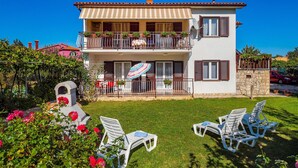 A two-story house with a balcony, a stone wall, and a lawn with lounge chairs. - Beautiful Home in Kapelica With Wifi and 2 Bedrooms (Labin)