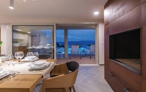 Ein Essbereich mit Tisch für vier Personen, eine Sitzgelegenheit am Pool und ein großer Fernseher an der Wand.