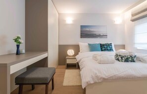 Ein modernes Schlafzimmer mit einem Bett, Nachttischen, einer Bank, einem Beistelltisch mit Lampe und Wandkunst.