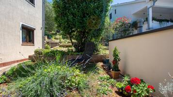 Un jardin avec différentes plantes et fleurs, une chaise et un bâtiment doté d’une fenêtre et d’un escalier.