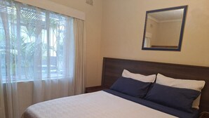 Una cama bien hecha con colcha blanca y azul, un cabecero de madera y una mesita de noche con lámpara.