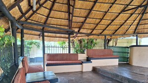 Un espacio de descanso al aire libre con bancos y una mesa, rodeado por una valla de metal y plantas.