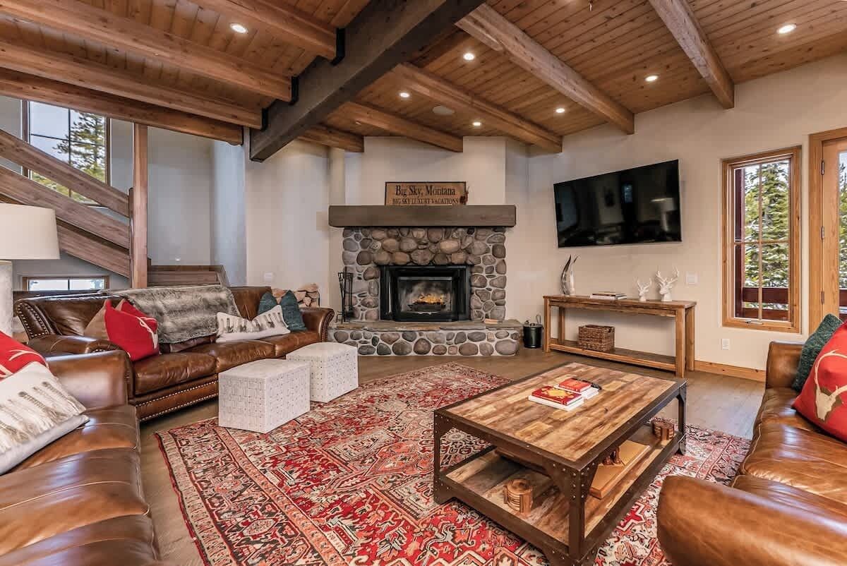 A cozy living room with a stone fireplace, leather sofas, a coffee table, and a large TV.