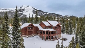 Un gran albergue de madera con varias habitaciones, rodeado de árboles cubiertos de nieve y montañas.