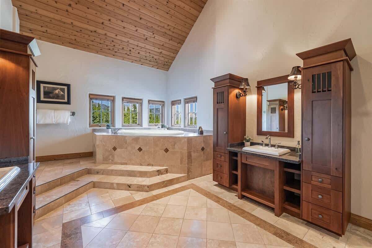 A spacious bathroom with a large bathtub, two sinks, and a wooden vanity.
