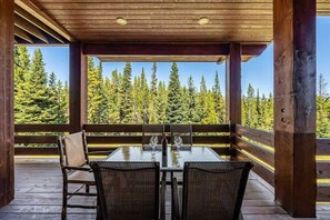 A covered outdoor seating area with a table and chairs, overlooking a forest.