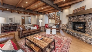 Amplia sala de estar con chimenea de piedra, sofás de cuero, una mesa de centro de madera y una escalera que conduce a un nivel superior.
