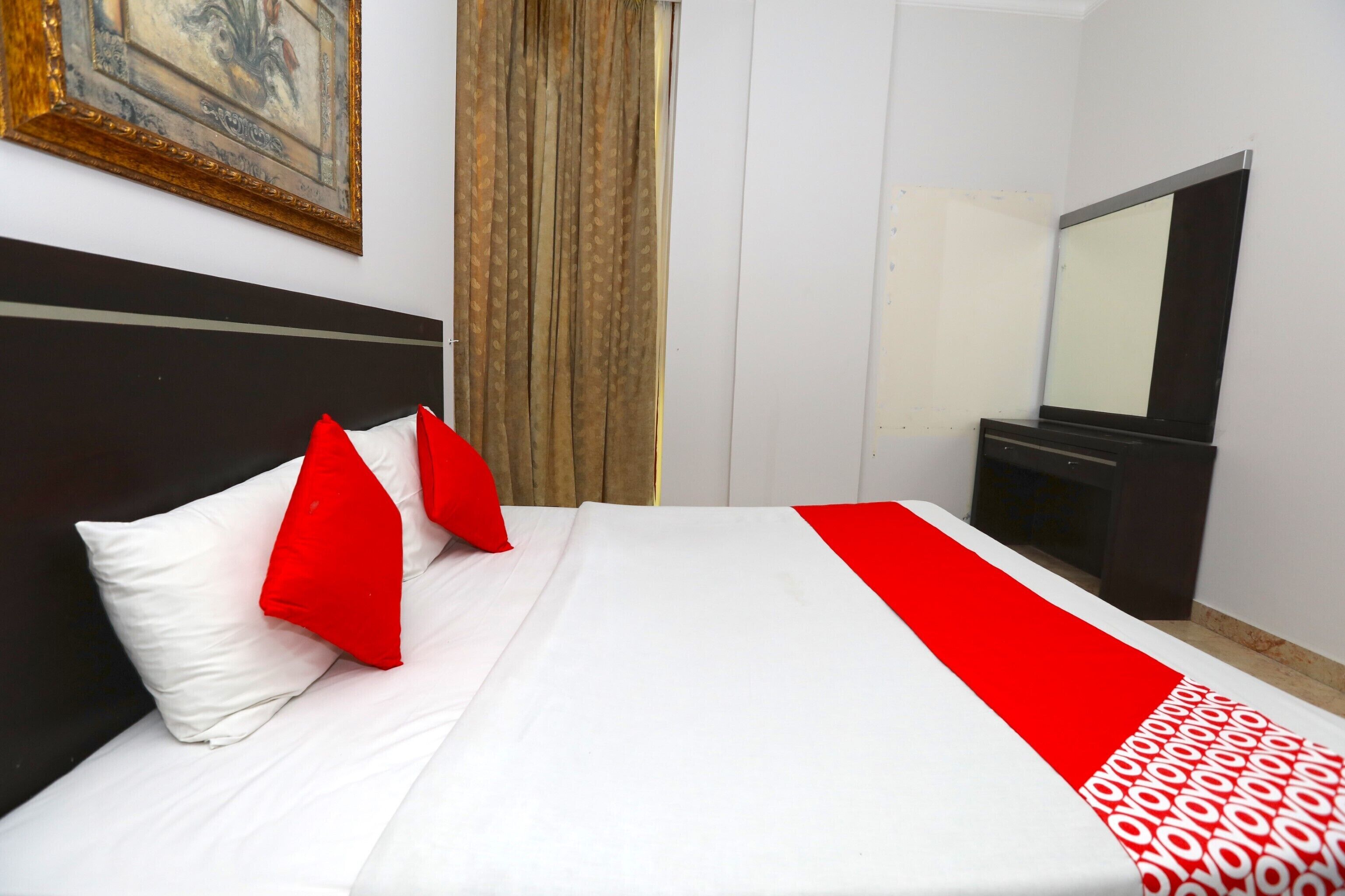 A hotel room with a neatly made bed, a large mirror, and a painting on the wall.