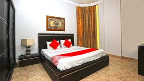 Una camera d'albergo con un letto grande, un comodino, una lampada, un quadro appeso al muro e una tenda.