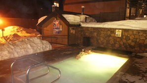 Un bain à remous avec un mur en pierre et un chalet en bois en arrière-plan.