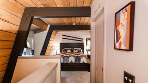 Une chambre avec un plafond en pente, un lit recouvert d’une couvre-lit à motifs, une tête de lit et un tableau accroché au mur.