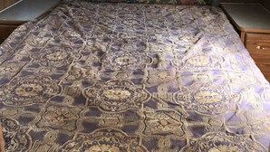 Een slaapkamer met een bed met een patroon, houten kasten met glazen deuren en een hoofdbord met decoratieve details.