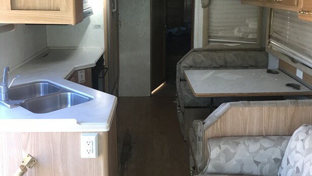 Een compact camperinterieur met een kitchenette, een eethoek en een slaapgedeelte.