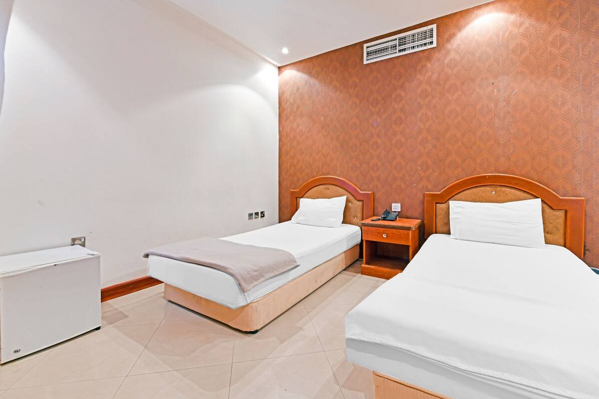 A hotel room with two single beds, a wooden headboard, a bedside table with a phone, and a radiator on the wall.