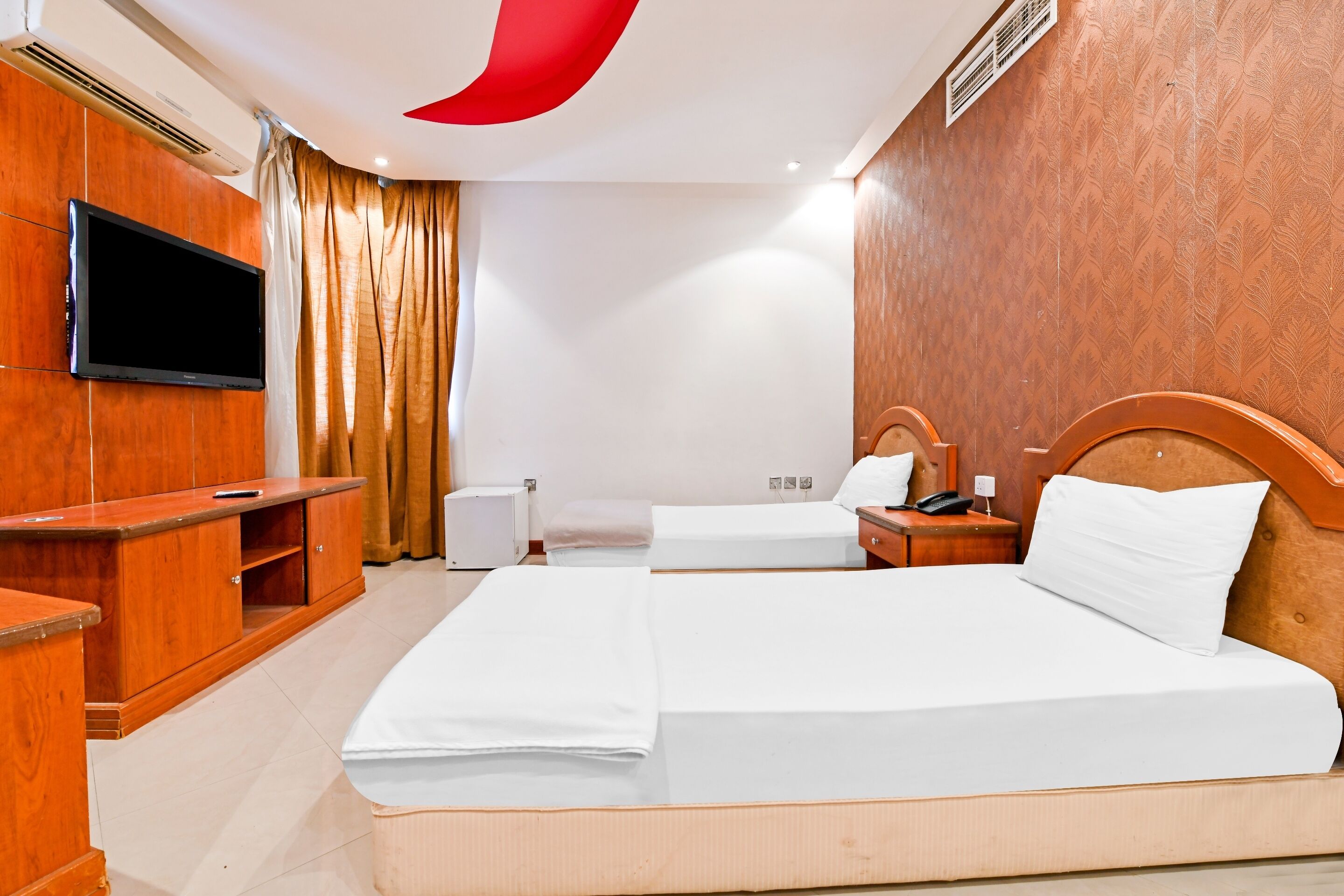 A hotel room with two beds, a TV, a wooden wardrobe, and a bedside table with a lamp.