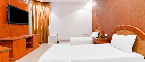 A hotel room with two beds, a TV, a wooden wardrobe, and a bedside table with a lamp.