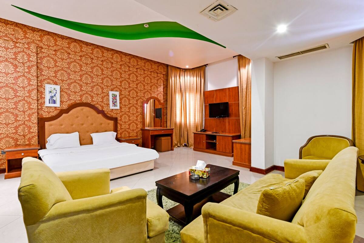 A hotel room with a large bed, a sofa, a coffee table, a TV, and a wooden cabinet.