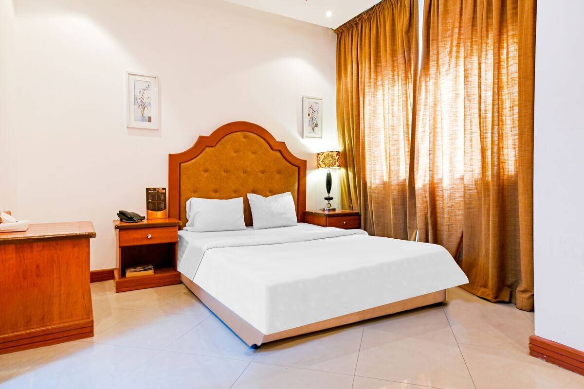 A hotel room with a large bed, wooden headboard, bedside tables, and a desk.