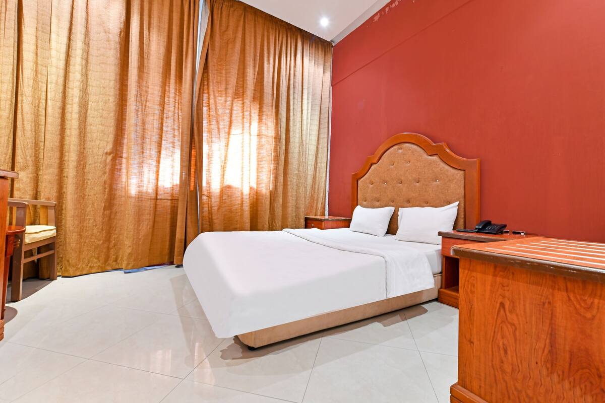 A hotel room with a large bed, wooden headboard, and a nightstand with a phone.