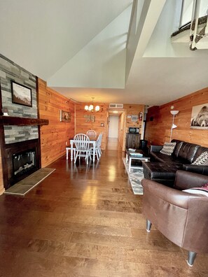 A spacious living area with a fireplace, wooden walls, a dining table with chairs, a leather sofa, and a TV.
