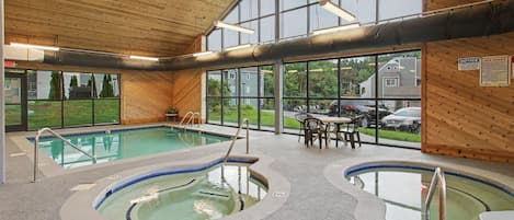 An indoor swimming pool area with multiple pools, a seating area, and large windows.