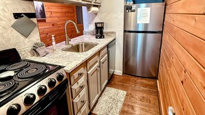 Una cocina con estufa, fregadero, refrigerador y paneles de madera en la pared.