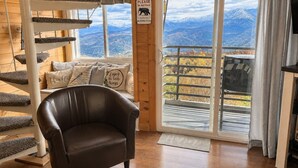 Una habitación con una escalera en espiral, un sillón de cuero, un sofá con cojines, un cartel sobre no alimentar osos y un gran ventanal con vistas a la montaña.