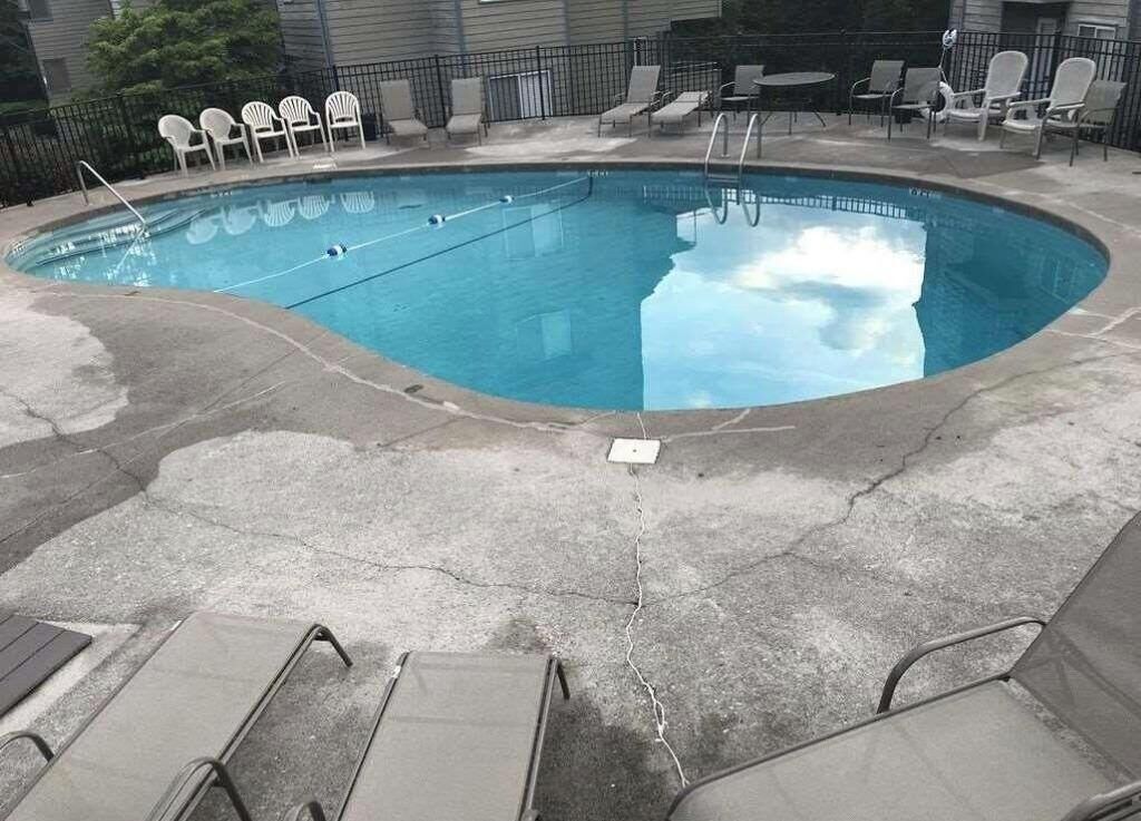 Una piscina con superficie de agua azul cristalina, rodeada de sillas de descanso y una plataforma de concreto.