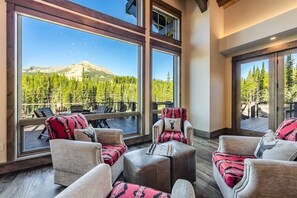 A spacious room with large windows overlooking a forested mountain. There are several chairs and a small table. - Alpine Lodge | Indoor Pool + Sports Court | Ski-In/Out (Big Sky)