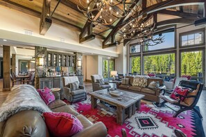 A spacious living area with a large chandelier, leather sofas, and a view of the outdoors through large windows.